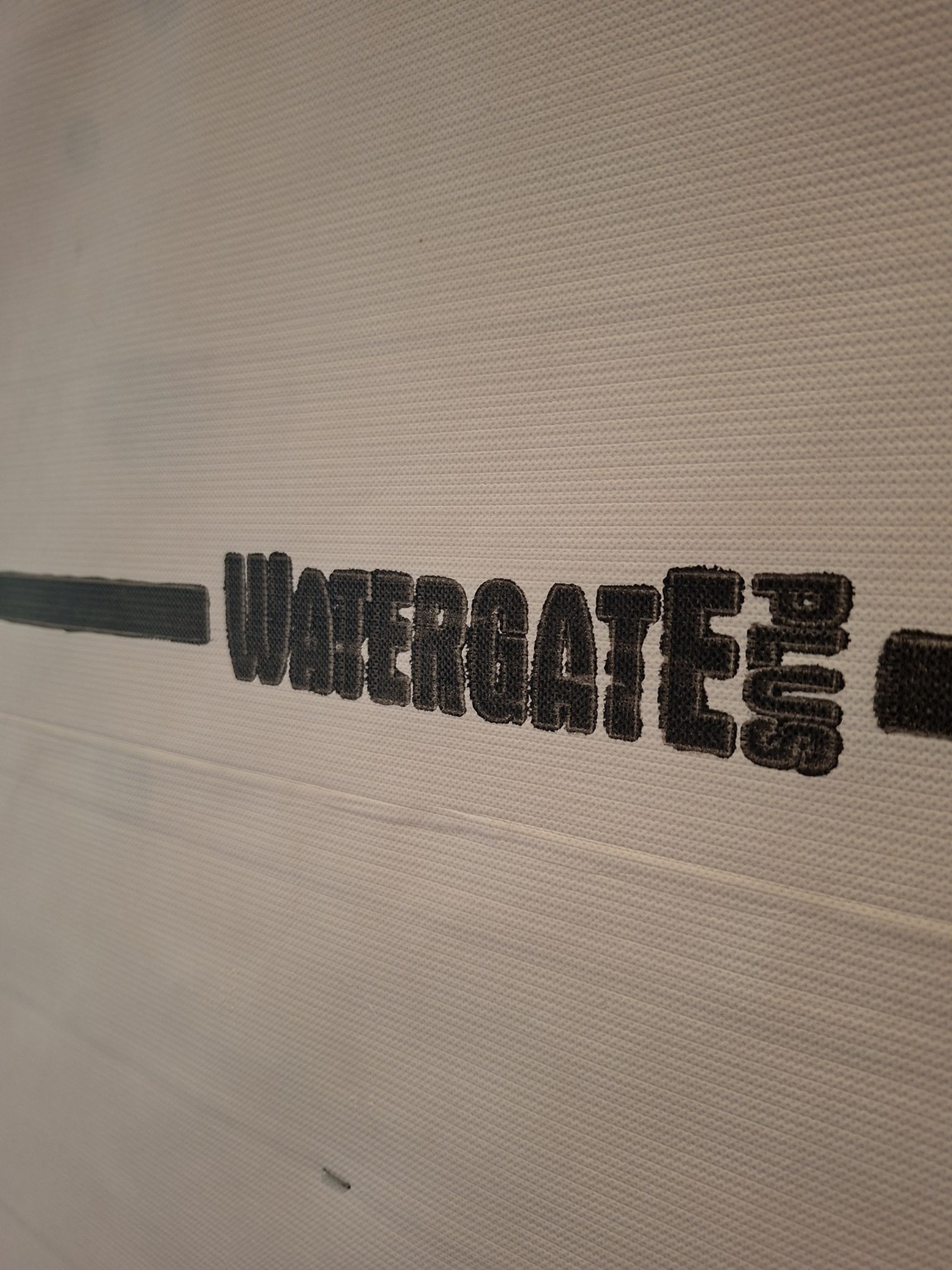 Black WATERGATE PLUS lettering on pale textured building wrap.